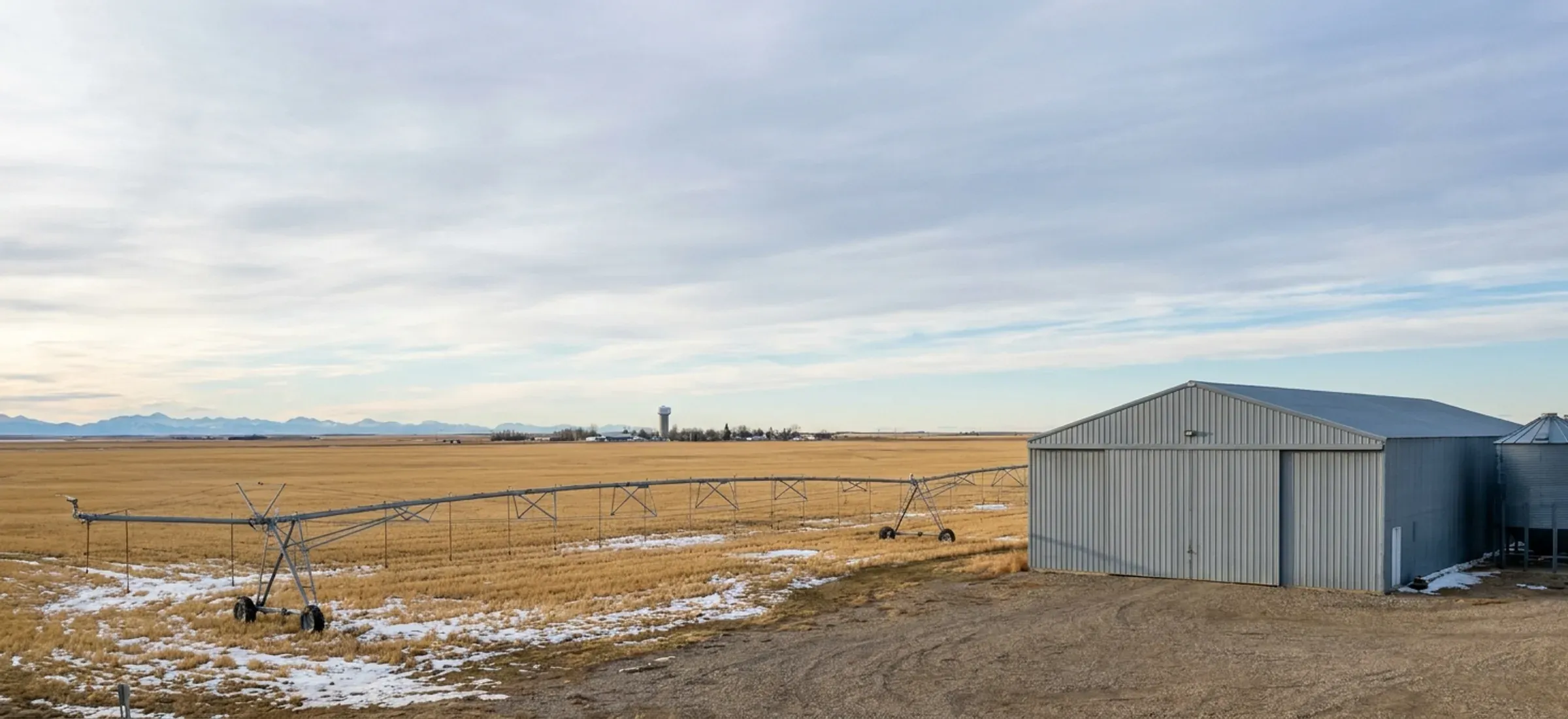 Flat irrigated farmland with a steel machine shed and grain bins under a wide prairie sky