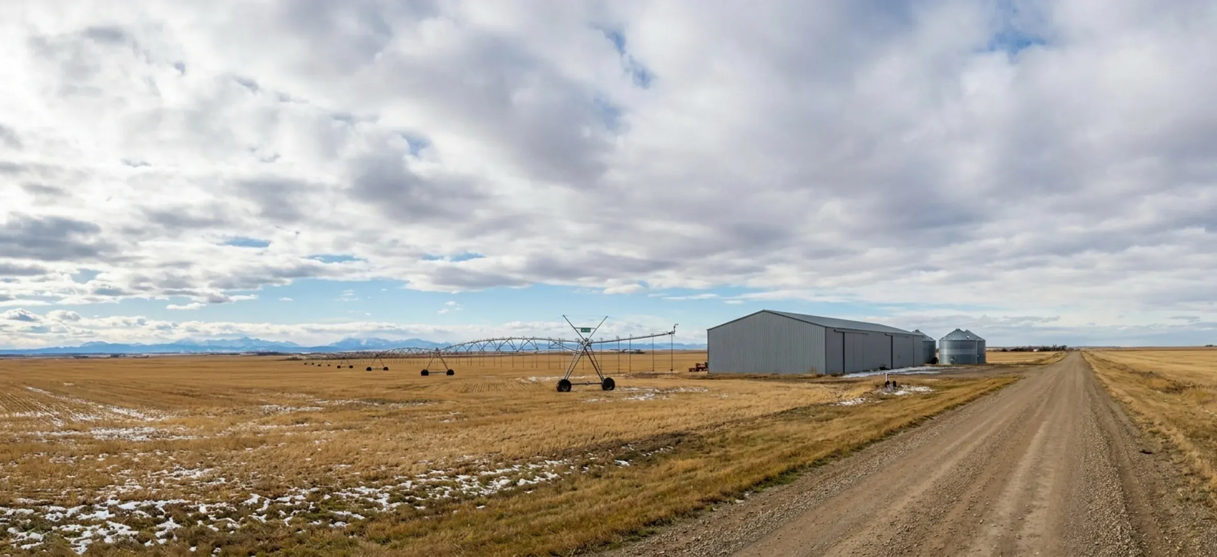 A steel machine shed set well back from a gravel road on flat irrigated farmland